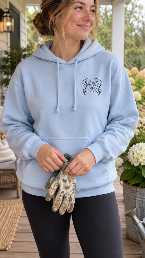 Light blue custom pet hoodie with a dog line-art portrait, worn on a porch while holding gardening gloves