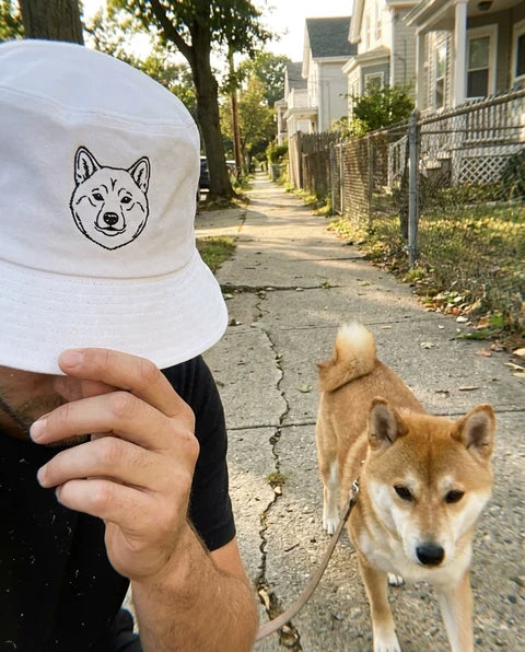 White custom pet bucket hat with a Shiba Inu line-art portrait, shown on a walk with a Shiba Inu
