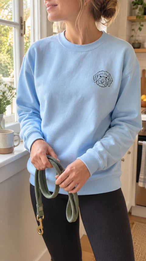 Light blue custom pet crewneck sweatshirt with a fine-line dog portrait, worn while holding a leash