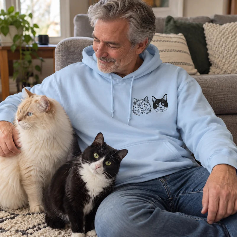 Light Blue hoodie with two cat portraits on the left chest, worn beside a cream long-haired cat and a tuxedo cat